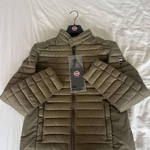 Olivgrön quiltad jacka från CMMN SWDN - Säljer en olivgrön quiltad jacka från CMMN SWDN. Jackan har en stilren design med dragkedja framtill och en hög krage. Perfekt för kyligare dagar med sin pufferstil och långa ärmar. En modern och funktionell jacka för garderoben. Jackan kostar endast 2000kr ny pris är 3500kr