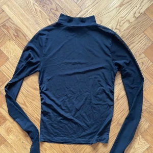 Svart topp i mesh - Svart långärmad topp i mesh. Hög krage och slimmad passform. Lite sliten i sidorna, men ingenting som syns med den på!