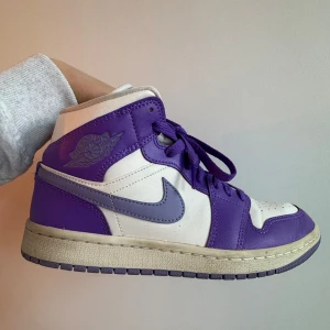 Nike Air Jordans i lila och vitt - Snygga Nike Air Jordans i en fräsch kombination av lila och vitt. Skorna har klassisk snörning och en ikonisk Nike-logga på sidan. Perfekta för dig som vill ha en stilren och sportig look.