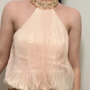 Champagnefärgad oneshoulderklänning - Elegant oneshoulderklänning i champagnefärg med glittriga paljettdetaljer på kjolen. Överdelen är plisserad och ger en lyxig känsla. Perfekt för festliga tillfällen.