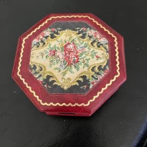Röd smyckesask med blommönster - Elegant röd smyckesask i oktagonal form med ett vackert blommönster på locket. Insidan är klädd i blått tyg och har en spegel. Perfekt för att förvara dina smycken med stil.