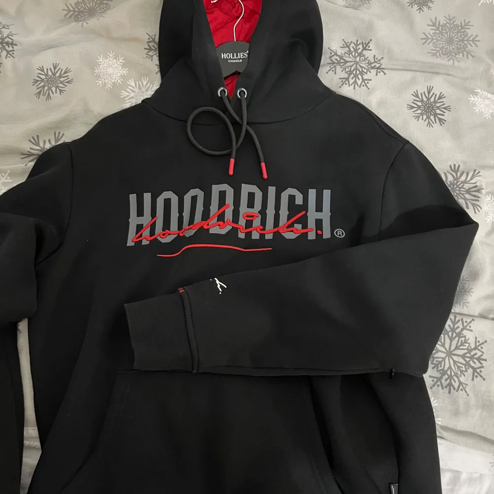 Säljer en svart hoodie från Hoodrich med röd och vit logga på bröstet. Hoodien har en justerbar huva med snören och en stor ficka framtill. Perfekt för en avslappnad stil. Pris kan diskuteras!!. Neuletakit & Villapaidat.