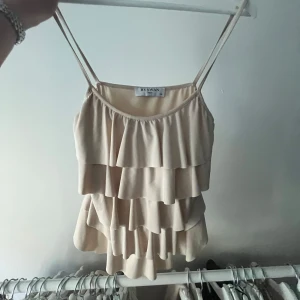 Beige volangtopp från By Swan - Säljer en söt beige topp från By Swan med volanger och smala axelband. Perfekt för varma dagar och ger en luftig känsla. Passar bra till både jeans och kjol.