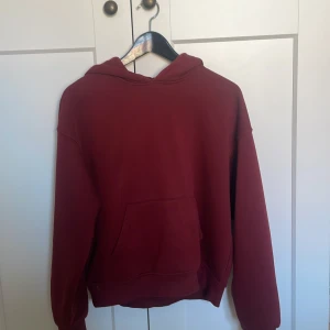 Vinröd hoodie från Gina Tricot - Säljer en vinröd hoodie från Gina Tricot, perfekt för en avslappnad stil. Den har en klassisk design med en stor ficka framtill och en bekväm huva. Passar perfekt för kyligare dagar.