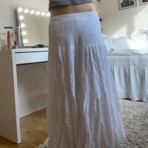 Vit långkjol - Säljer en vacker vit långkjol med en luftig och flödande design. Kjolen har en elastisk midja för bekväm passform och är perfekt för varma dagar. Den är gjord i ett lätt material som ger en skön känsla. Perfekt för en avslappnad och stilren look.