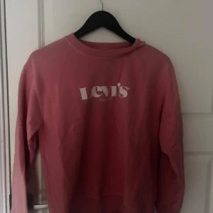 Rosa långärmad tröja från Levi's - Säljer en rosa långärmad tröja från Levi's med deras klassiska logga tryckt på framsidan. Perfekt för en avslappnad stil och enkel att matcha med jeans eller kjol.
