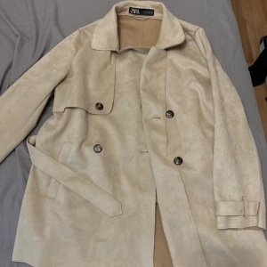 Beige trenchcoat från Zara - Snygg beige trenchcoat från Zara med klassisk design. Jackan har knappar framtill och ett bälte i midjan. Som ny!