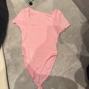 Rosa bodysuit - Säljer en söt rosa bodysuit med korta ärmar och fyrkantig halsringning. 
