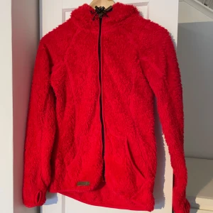 Röd teddy tjocktröja från McKinley - Säljer en supermjuk och varm röd teddyjacka från McKinley. Jackan har en dragkedja framtill och en mysig huva. Perfekt för kyliga dagar när du vill hålla dig varm och bekväm. 🧥
