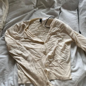 Beige kofta från H&M - Säljer en stilren beige kofta från H&M. Den har långa ärmar och knappar framtill. Koftan är inte så skrynklig som den ser ut!!!