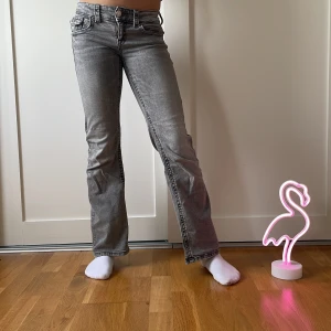 Grå gina jeans bootcut  - Snygga grå bootcut jeans med medel/låg midja och klassiska femficksdetaljer. Jeansen har en stilren design med knappar och dragkedja framtill. Perfekta för en avslappnad look.