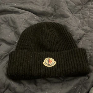 Svart ribbad mössa från Moncler - Snygg svart ribbad mössa från Moncler med broderad logotyp framtill. Perfekt för att hålla värmen under kyliga dagar. Stilren design som passar till det mesta. Tveka inte om ni har någon fråga! Mvh Alvin 