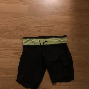 Svarta träningsshorts med grön midja - Snygga svarta träningsshorts med en kontrasterande grön midja och snörning. Perfekta för gymmet eller löprundan. De har en bekväm passform och är gjorda i ett lätt och andningsbart material.