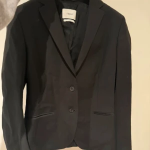 Svart kavaj från Filippa K - Elegant svart kavaj från Filippa K med klassisk design. Kavajen har två knappar framtill och smal passform. Perfekt för en stilren look. Frakt tillkommer!