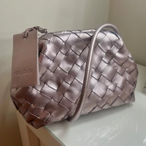 Intressekoll!!! Cala Jade väska 💓 - Intressekoll! Ge prisförslag! ⭐️ världens finaste clutch väska från Cala Jade!!! Asså dröm väskan!!!!! 🩷🩷 Säljer endast vid bra bud 💕modellen heter AIMEE och färgen är rose metallic och är sååå unik och snygg 😍 aldrig använd med lappar kvar, köpt på Åhléns för knappt en månad sen