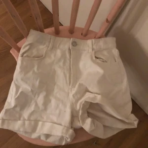Vita shorts från H&M - Säljer ett par vita shorts från H&M. De är högmidjade med knapp och dragkedja framtill. Shortsen har fickor både fram och bak, vilket ger en klassisk look. Perfekta för varma dagar!