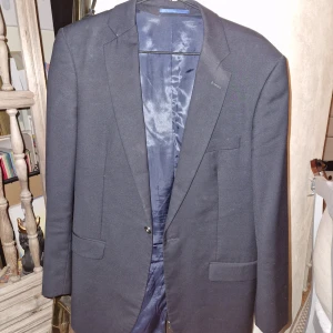 Svart kavaj från Dressmann - Snygg svart kavaj från Dressmann, perfekt för en stilren look. Kavajen har klassiska drag och två knappar framtill. Passar utmärkt till både formella och semi-formella tillfällen.