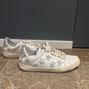 Vita sneakers med silverstjärnor från Zadig & Voltaire - Snygga vita sneakers från Zadig & Voltaire med coola silverstjärnor på sidorna. Skorna har en klassisk snörning och en bekväm passform. Perfekta för att ge din outfit en extra touch av stil.