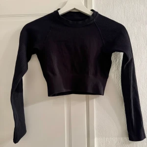 Svart ribbad croppad tröja - Snygg svart ribbad tröja med lång ärm och croppad design. Tillverkad i Italien av 96% polyamid och 4% elastan för en stretchig passform. Perfekt för en stilren look till gymmet.