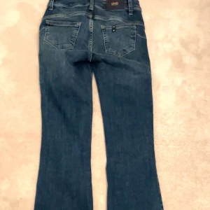 Blå bootcut jeans - MIDJEMÅTT: 35cm tvärsöver. INNERBENSLÄNGD: 80cm Snygga blå bootcut jeans med klassisk femficksdesign. De har en mörk tvätt och en liten etikett på bakfickan. Perfekta för en avslappnad stil.