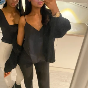 Svart satin linne med tunna axelband - Snyggt svart satin linne med tunna axelband och v-ringning. Perfekt för en stilren look. Passar bra till både jeans och kjol.