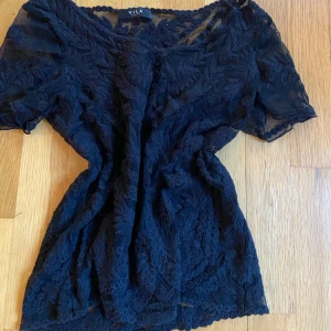 Svart spetsblus från Vila - Säljer en elegant svart spetsblus från Vila. Blusen har korta ärmar och ett vackert spetsmönster som ger en romantisk känsla. Perfekt för att lyfta vilken outfit som helst. Passar bra till både jeans och kjol.