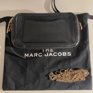 Svart axelväska från Marc Jacobs - Marc Jacobs softshot leather handbag. Snygg svart axelväska från Marc Jacobs i skinn med guldfärgade detaljer. Väskan har en praktisk dragkedja och en kedja som axelrem. Perfekt för att bära dina nödvändigheter med stil.