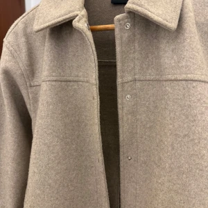 Beige jacka från Vero Moda - Säljer en stilren beige jacka från Vero Moda i storlek XS, men den är rymlig i modellen och passar även dig som vanligtvis bär S. Jackan har en klassisk krage och knäppning framtill, vilket gör den till ett perfekt val för en elegant och tidlös look.