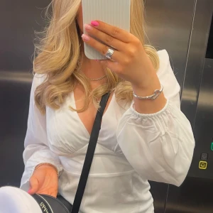 STUDENTKLÄNNING - Säljer en elegant vit omlottklänning med långa ärmar och v-ringning. Klänningen har en figurnära passform och är perfekt för studenten. Den är både stilren och bekväm. Storlek 36. Endast använd 1 tillfälle 