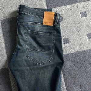 Blå jeans från Jack & Jones - Snygga blå jeans från Jack & Jones i modellen Slim/Glenn. De har en klassisk femficksdesign och en läderpatch med logotyp baktill. Perfekta för en stilren look. Bra skick och de är i storlek 32/32!