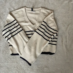 Beige och svart randig tröja från H&M Divided - Säljer en snygg beige tröja från H&M Divided med svarta ränder. Tröjan har en v-ringad hals och långa ärmar. Perfekt för en stilren look. 