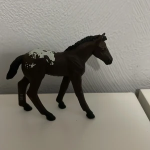 Leksaks häst  - Detaljerad brun hästfigur med vita fläckar på ryggen. Perfekt för samlare eller som leksak för hästälskare. Figuren har en realistisk design med noggrant utformade detaljer.