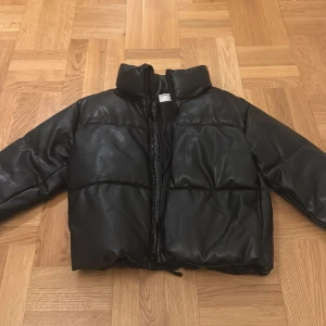 Svart pufferjacka från Old Navy - Säljer en svart pufferjacka från Old Navy i syntetiskt läder. Jackan har en dragkedja framtill och en hög krage för extra värme. Perfekt för kyliga dagar och ger en cool look. 🖤