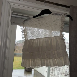 Beige spetstopp från Zara - Säljer en söt beige ärmlös topp från Zara. Toppen har spetsdetaljer och volanger som ger en romantisk känsla. 