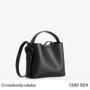 Svart crossbody-väska - Snygg svart crossbody-väska från Arket med stilren design. Väskan har ett justerbart axelband och är perfekt för att för att bära dina dagliga nödvändigheter.  Tillverkat i ett hållbart material och ger en elegant look. 