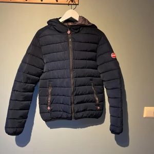 Mörkblå pufferjacka från Colmar - Säljer en snygg mörkblå pufferjacka från Colmar med dragkedja och huva. Jackan har ett quiltat mönster och två praktiska fickor med dragkedjor. Perfekt för kyliga dagar. Säljer denna snygga jacka pga att den blivit för liten för mig🙁 