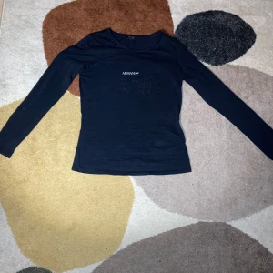 Svart långärmad topp från Armani Jeans - Snygg svart långärmad topp från Armani Jeans med glittrande text på framsidan. Perfekt för en stilren look. Tillverkad i mjukt material för extra komfort. Använt 1-2 gånger MAX. 