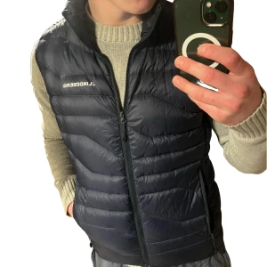 Marinblå dunväst J.Lindeberg - Snygg marinblå dunväst från J.Lindeberg med trasig dragkedja framtill som lätt och billigt går att laga för 10kr! Har bara inte orkat då den ändå var för liten. I övrigt mycket fint skick utan defekter. Modell cliff light down vest som kostar 2000kr ny. Storlek S