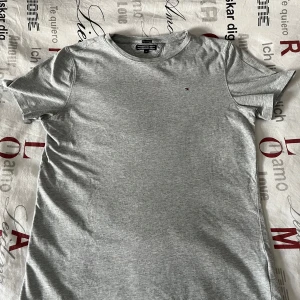Grå t-shirt från Tommy Hilfiger - Säljer en stilren grå t-shirt från Tommy Hilfiger. Den har en liten broderad logga på bröstet och är tillverkad i mjukt bomullsmaterial. Perfekt för en avslappnad look. T-shirten är använd mycket men är fortfarande i bra skick 