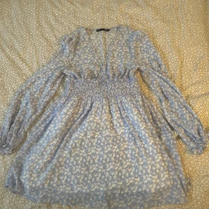 Blommig blå klänning från lager 157 - Charmig blå klänning med blommigt mönster från lager 157. Den har en smickrande v-ringning och långa ärmar. Midjan är elastisk för en bekväm passform. Perfekt för vår och sommar! Inga synliga defekter. är som ny!🌸