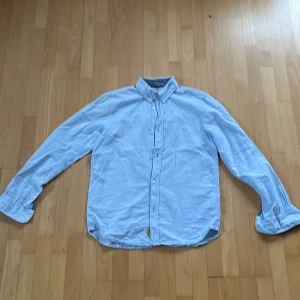 Ljusblå skjorta från L.O.G.G. - Säljer en stilren ljusblå skjorta från L.O.G.G. med klassisk krage och knappar framtill. Skjortan har långa ärmar och är perfekt för en avslappnad men ändå uppklädd look. Passar bra till både jeans och chinos.