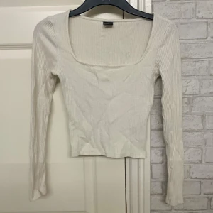 Vit ribbad topp från H&M - Säljer en stilren vit ribbad topp från H&M med långärmad design och fyrkantig halsringning. Perfekt för lager-på-lager eller som den är. Passar till många olika stilar och tillfällen.