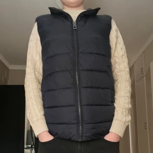 Svart Väst från Indicode - Säljer en helt ny snygg svart dunväst från Indicode på grund av dubbelköp från Zalando. Västen har en dragkedja framtill och är perfekt för kyligare dagar. Den är quiltad för extra värme och stil. Passar bra till både casual och mer uppklädda tillfällen. 