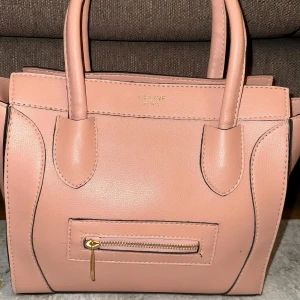 Rosa handväska - Snygg rosa handväska i skinnimitation. Väskan har två handtag och stilrena detaljer.