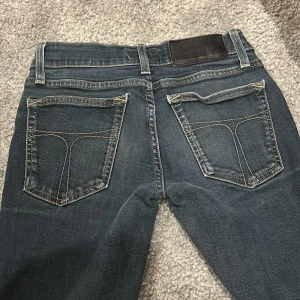 Mörkblå jeans från Tiger of Sweden - Snygga mörkblå jeans från Tiger of Sweden med klassisk femficksdesign och guldfärgade sömmar. Jeansen har en dragkedja och knapp framtill samt en läderpatch på baksidan av midjan. Inga hål eller form av slitning 