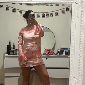 Rosa mönstrad klänning med öppen rygg - Trendig rosa klänning med abstrakt mönster och öppen rygg. Den har långa ärmar och en knytning i nacken. Perfekt för en stilfull look.