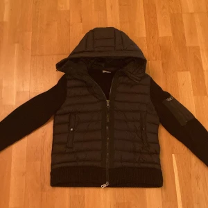 Moncler cardigan  - Säljer en svart jacka från Moncler med huva och dragkedja. Jackan har långa ärmar och ett quiltat mönster på framsidan. Perfekt för kyligare dagar med stil.