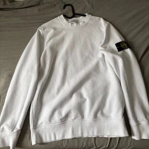 Stone Island tröja - Säljer en stilren vit tröja från Stone Island med deras ikoniska märke på ärmen. Köpt för 3000kr men inte använd så ofta, inga skador eller fläckar eller liknande.