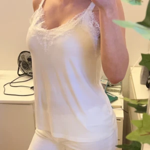 Vit linne med spetsdetaljer - Säljer ett stilrent vitt linne med spetsdetaljer vid halsringningen. Linnet har smala axelband och en mjuk, följsam passform. Perfekt för varma dagar eller som ett lager under andra plagg.