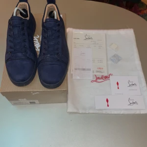 Mörkblå sneakers från Christian Louboutin - Snygga mörkblå sneakers från Christian Louboutin med den ikoniska röda sulan. Skorna har snörning och är tillverkade i mocka. Perfekta för den som vill ha en stilren och lyxig look. 